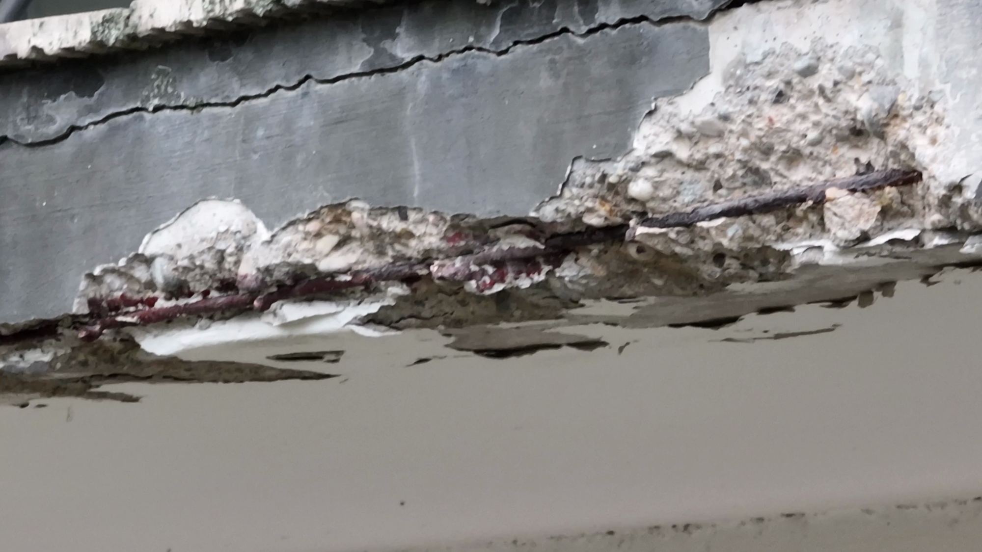 Nahaufnahme der Abplatzung mit freiliegender, rostiger Bewehrung und Rissen im Beton