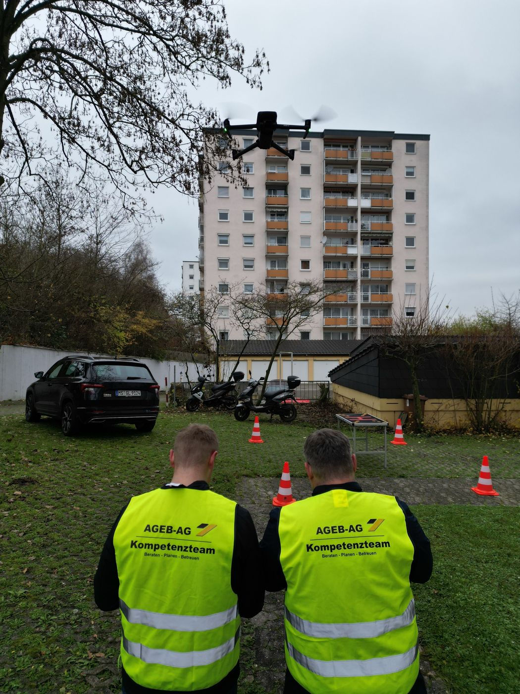 Zwei Teammitglieder in Warnwesten beobachten die Drohne vor einem Wohnhochhaus