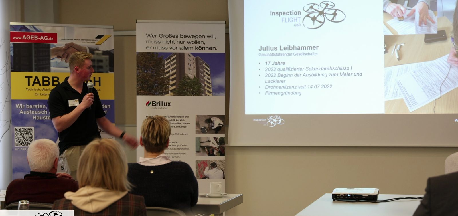 Julius Leibhammer bei einem Vortrag vor Publikum, im Hintergrund die Präsentation